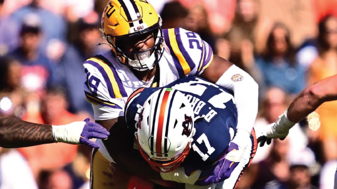LSU player in a yellow helmet tackles Alabama player in navy uniform during a college football game.