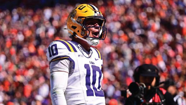 LSU football player in white jersey number 10 with a yellow helmet on the field, shouting during a game