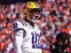 LSU football player in white jersey number 10 with a yellow helmet on the field, shouting during a game