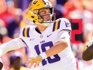LSU quarterback in white jersey #10 and yellow helmet throwing a pass during a game.