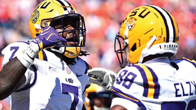 Two LSU football players in white jerseys and yellow helmets face off on the field during a game.