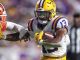 LSU running back (#13) cradles the football as a Clemson defender closes in during a college football play.
