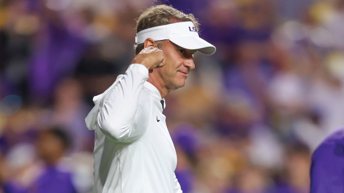 Coach or athlete wearing a white polo and visor on a sports field, cupping his ear toward the crowd.
