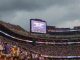 Packed football stadium with fans in purple; scoreboard reads 'Lightning Delay' during the event pause.