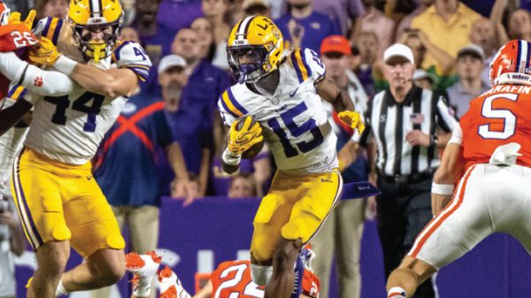LSU player wearing number 15 runs with the ball as Florida defenders attempt to tackle; crowd and referee in background.