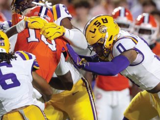 LSU players in purple and gold tackle a Florida Gators player in orange during a college football game.