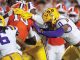 LSU players in purple and gold tackle a Florida Gators player in orange during a college football game.