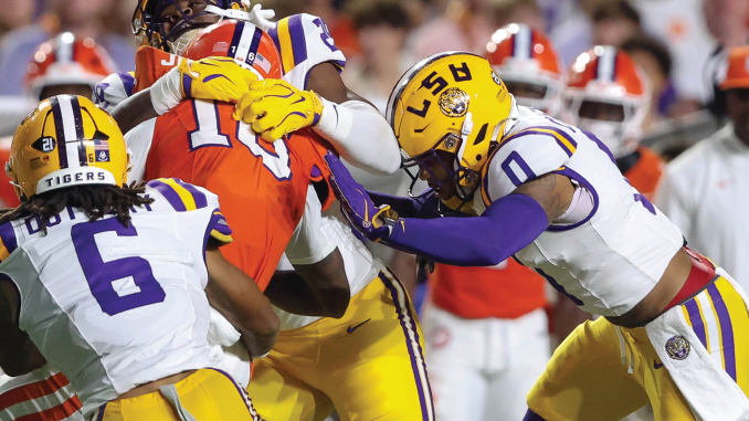 LSU players in purple and gold tackle a Florida Gators player in orange during a college football game.