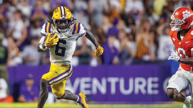 LSU running back wearing number 6 sprints with the football, pursued by Clemson defender in orange jersey on a crowded field.