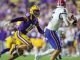 LSU defender in purple and gold (#10) chases a quarterback in white and red on a bright game day field.