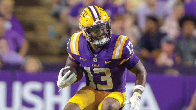 LSU football player in purple and gold jersey number 13 running with the ball on the field at a game stadium