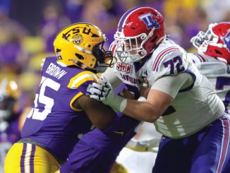 College football players collide at the line: a purple-and-gold defender (#65) tackles a white-jersey opponent with a red helmet.