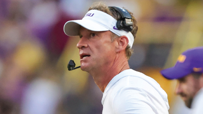 Football coach on the sideline wearing a white visor and headset, looking off to the right.