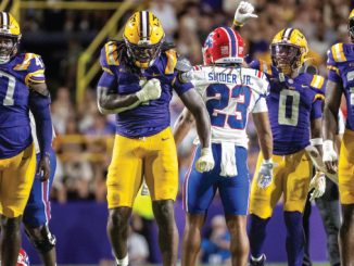 Group of LSU football players in purple and gold celebrate on the field as a Bills opponent wearing #23 walks away in the middle.