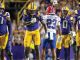 Group of LSU football players in purple and gold celebrate on the field as a Bills opponent wearing #23 walks away in the middle.