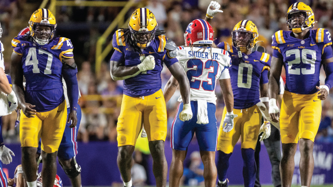Group of LSU football players in purple and gold celebrate on the field as a Bills opponent wearing #23 walks away in the middle.