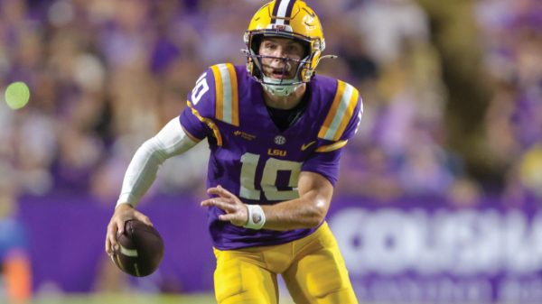 LSU Tigers quarterback wearing purple and gold, number 10, running with the football during a game.