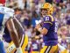 LSU quarterback in purple and gold (#10) prepares to throw a pass during a football game against the Bills, crowd in background.