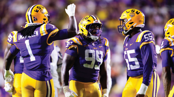 LSU football players celebrate on the field in purple and gold, giving high-fives amid a crowd.
