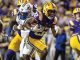 LSU Tigers running back in purple and gold carries the football as defenders chase during a college football game.