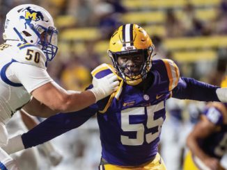 LSU linebacker wearing purple and gold, #55, being tackled by Michigan defender #50 in white during a college football game on a crowded field.