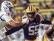 LSU linebacker wearing purple and gold, #55, being tackled by Michigan defender #50 in white during a college football game on a crowded field.