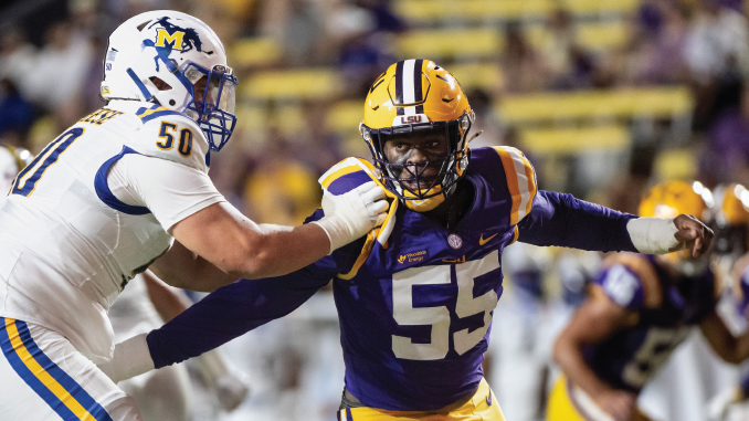 LSU linebacker wearing purple and gold, #55, being tackled by Michigan defender #50 in white during a college football game on a crowded field.