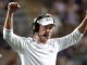 LSU football coach on the sideline, wearing a white long-sleeve shirt and visor, arms raised in celebration.