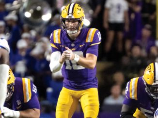 LSU quarterback in purple and gold prepares to throw, during a game under bright stadium lights.