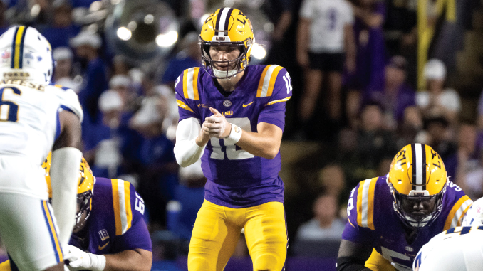 LSU quarterback in purple and gold prepares to throw, during a game under bright stadium lights.
