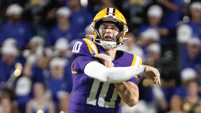American football quarterback in purple and gold uniform throwing a pass during a game in front of a cheering crowd.