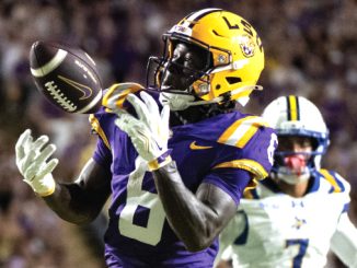 LSU Tigers football player in purple and gold catching a pass during a game, ball secured in midair.