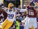 LSU defender in white jersey #29 with yellow pants reaches to tackle during a college football play against Alabama, with a Puckett #15 Alabama player nearby and fans in the background.