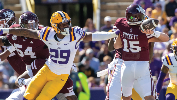 LSU defender in white jersey #29 with yellow pants reaches to tackle during a college football play against Alabama, with a Puckett #15 Alabama player nearby and fans in the background.