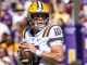 LSU quarterback in white and purple jersey number 10 holding a football, looking downfield during a game.