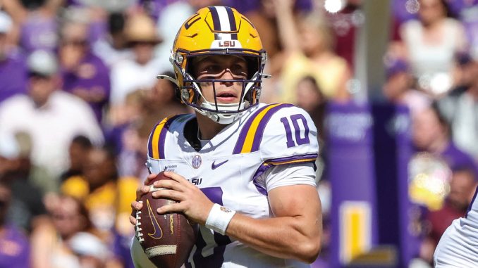 LSU quarterback in white and purple jersey number 10 holding a football, looking downfield during a game.