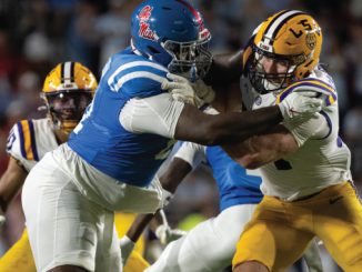Ole Miss running back stiff-arms LSU defender during a college football game on a night stadium field