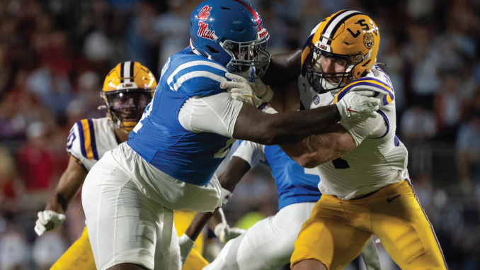 Ole Miss running back stiff-arms LSU defender during a college football game on a night stadium field