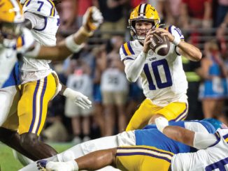 LSU quarterback #10 throwing a pass while defenders close in during a football game.