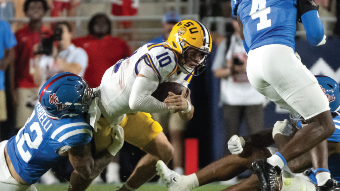 LSU running back carries the football while an Ole Miss defender tackles him during a college football game.