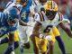 LSU Tigers running back wearing number 6 sprints with the ball, chased by blue-clad defenders during a game on the field.