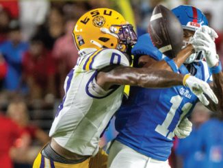 Two football players collide: a blue‑jersey receiver with helmet number 1 is tackled by a yellow‑helmet defender during a catch attempt.