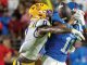 Two football players collide: a blue‑jersey receiver with helmet number 1 is tackled by a yellow‑helmet defender during a catch attempt.