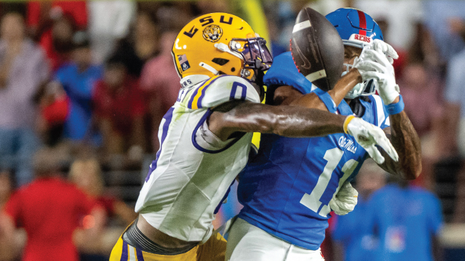 Two football players collide: a blue‑jersey receiver with helmet number 1 is tackled by a yellow‑helmet defender during a catch attempt.