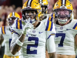 Two LSU football players celebrate on the field, white uniforms with purple numbers 2 and 7 and yellow helmets.