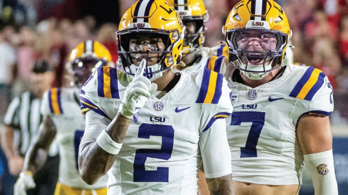 Two LSU football players celebrate on the field, white uniforms with purple numbers 2 and 7 and yellow helmets.