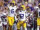 LSU Tigers football players in white jerseys and yellow pants celebrate on the field, with #6 pointing and #42 standing beside, as other teammates celebrate nearby.