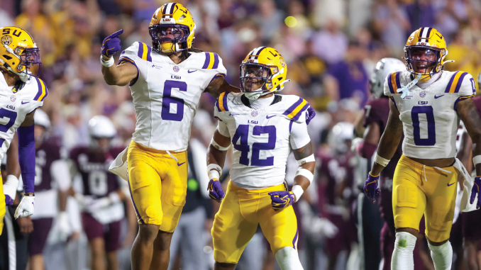 LSU Tigers football players in white jerseys and yellow pants celebrate on the field, with #6 pointing and #42 standing beside, as other teammates celebrate nearby.