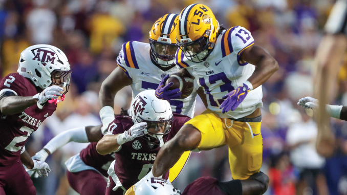 LSU ball carrier in white and yellow jumps over Texas A&M defenders during a crowded college football play.