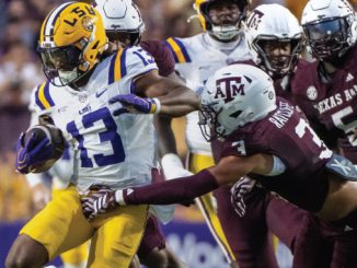 LSU running back #13 carries the ball, dodging Texas A&M defenders during a tight college football play.